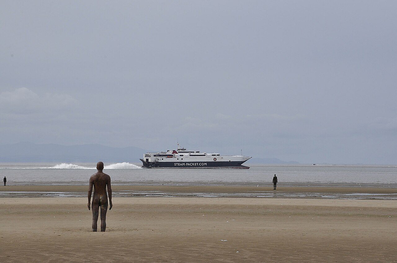 One of the Another Place iron figures on Crosby Beach looking out to sea, with a ship on the horizon