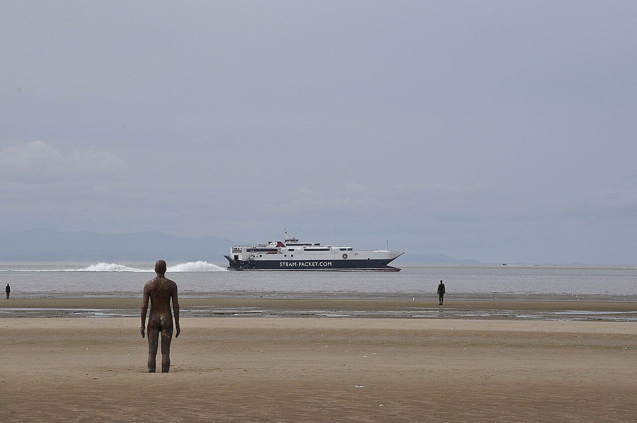 One of the Another Place iron figures on Crosby Beach looking out to sea, with a ship on the horizon