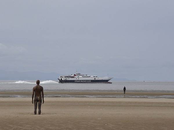 One of the Another Place iron figures on Crosby Beach looking out to sea, with a ship on the horizon